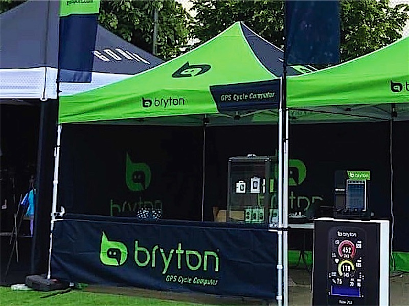 Carpas plegables con banderas y mostrador de una marca de ciclismo en un evento al aire libre.