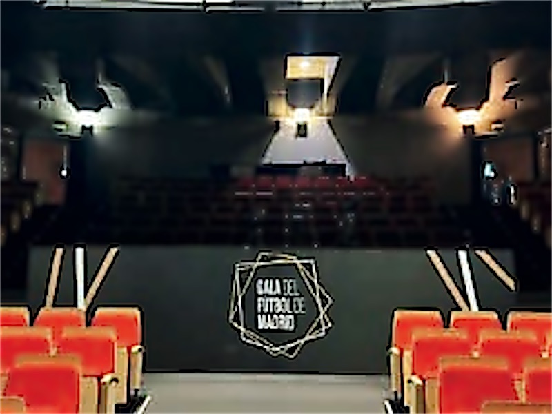 Escenario de un auditorio preparado para una gala, con el logotipo al fondo.