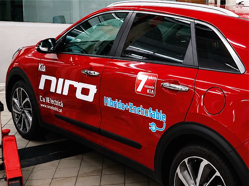 Coche híbrido rojo con vinilos de marca y de campaña en las puertas.